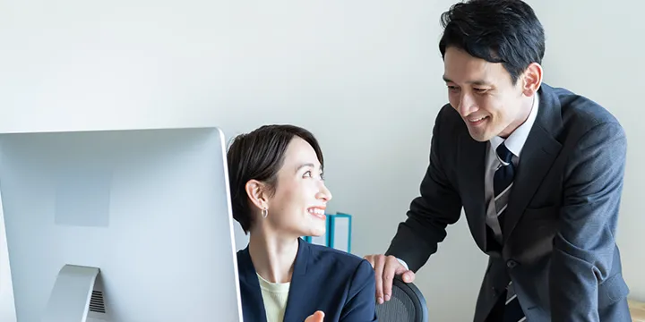PCの画面を前に談笑する二人のビジネスパーソン